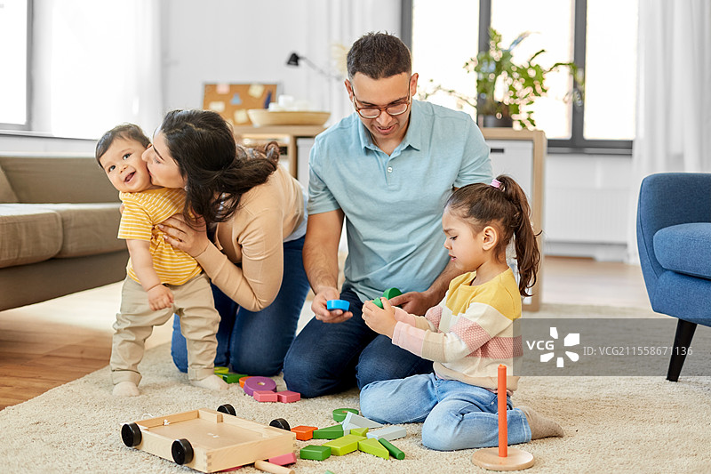 家庭和人们的概念 - 快乐的母亲、父亲、小女儿和婴儿儿子在家里玩木制玩具。快乐的家庭在家里玩木制玩具。图片素材