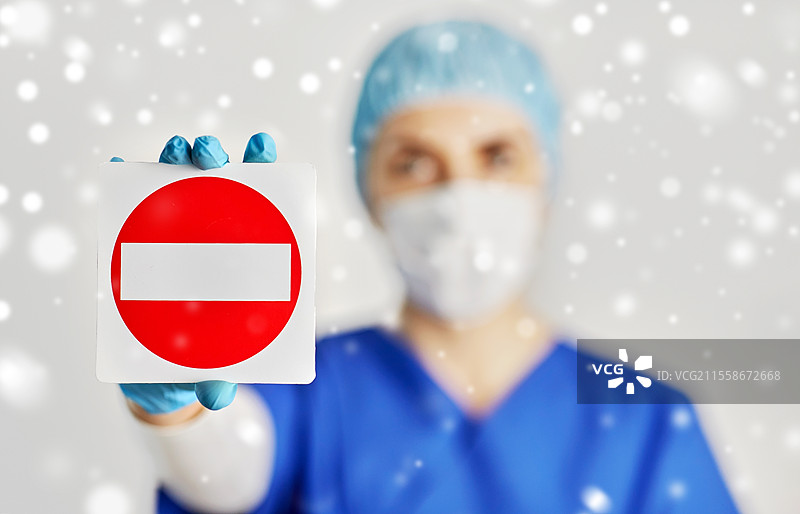 健康、医学和疫情概念 - 年轻女性医生或护士戴着防护口罩以防止病毒疾病，头戴帽子，在冬季雪地中展示停止手势。戴着口罩的医生或护士展示停止手势。图片素材