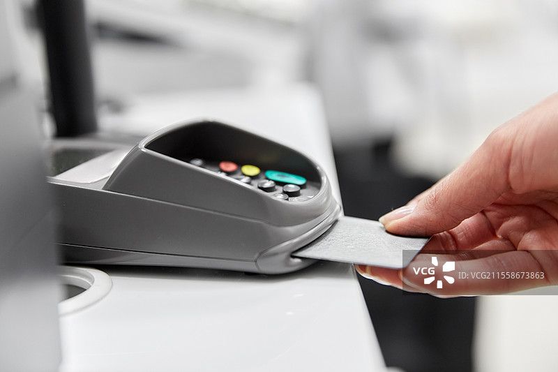 购物、支付和金融概念 - 手握信用卡靠近刷卡机的特写。图片素材
