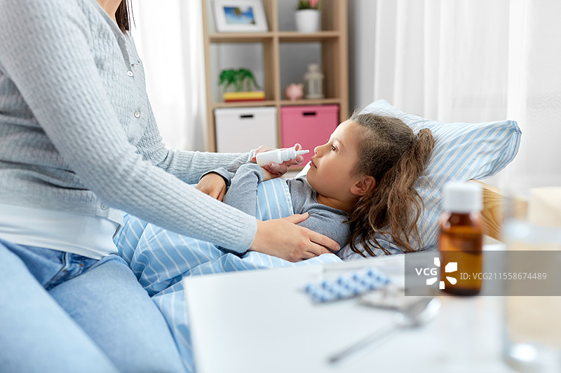家庭、健康与医学概念 - 母亲用鼻喷雾剂为躺在床上的小女儿治疗。母亲用鼻喷雾剂照顾生病的女儿。图片素材