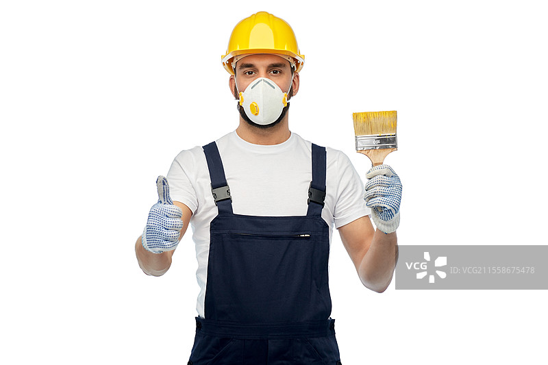 职业，建筑和施工 - 戴着黄色安全帽和防毒面具的男性工人或建筑工人，手持刷子，竖起大拇指，背景为白色。戴着防毒面具的建筑工人手持刷子，竖起大拇指。图片素材