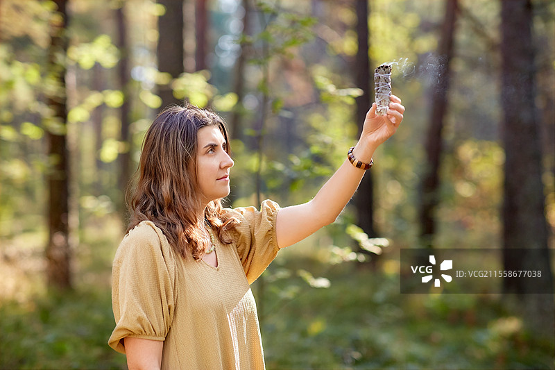 神秘科学与超自然概念 - 年轻女性或女巫在森林中用冒烟的白鼠尾草进行魔法仪式。女性或女巫在森林中进行魔法仪式。图片素材