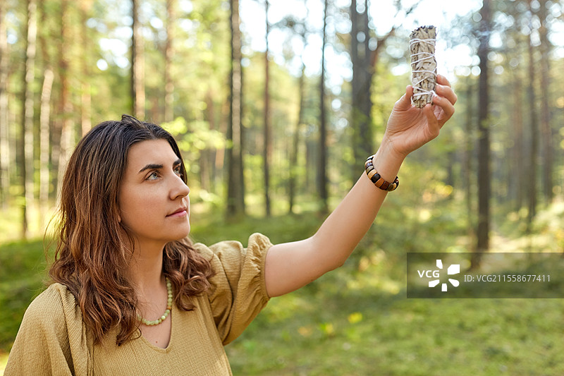 神秘科学与超自然概念 - 年轻女性或女巫在森林中用冒烟的白鼠尾草进行魔法仪式。女性或女巫在森林中进行魔法仪式。图片素材