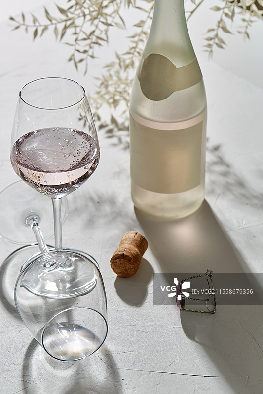 饮品、酒精和玻璃器皿概念 - 红酒杯和打开的香槟瓶在白色表面上投下阴影。红酒杯和香槟瓶投下的阴影。图片素材