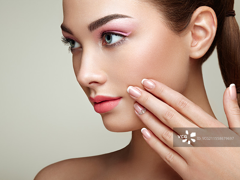 美丽的棕发女性，妆容完美。粉色的嘴唇和指甲。完美的眉毛。护肤粉底。美丽女孩的面孔独立于米色背景。手部有着优雅的美甲。图片素材