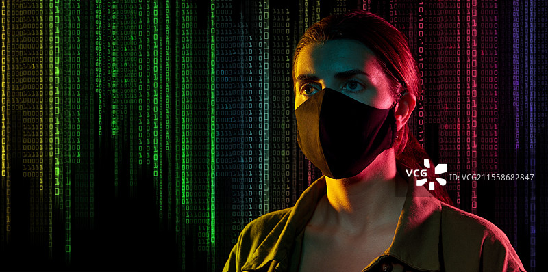 网络犯罪、黑客和技术概念 - 年轻女性黑客戴着黑色面具，背景是黑色的二进制代码数字。戴着黑色面具的女性黑客与二进制代码。图片素材