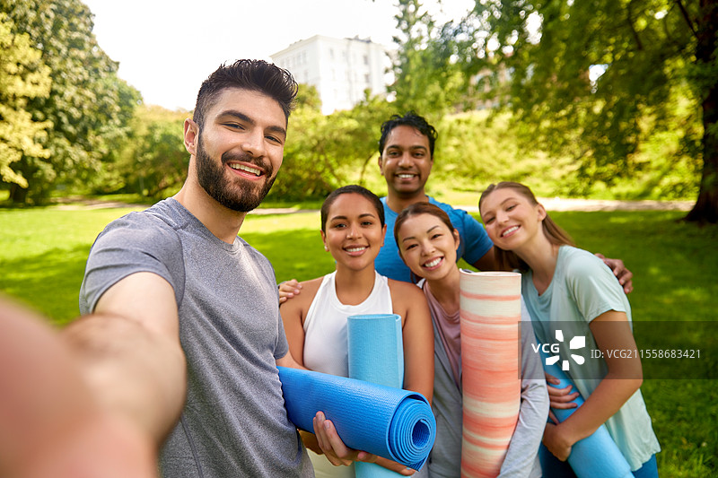 健身、运动和健康生活方式的概念 - 一群快乐的人在公园用瑜伽垫自拍。图片素材
