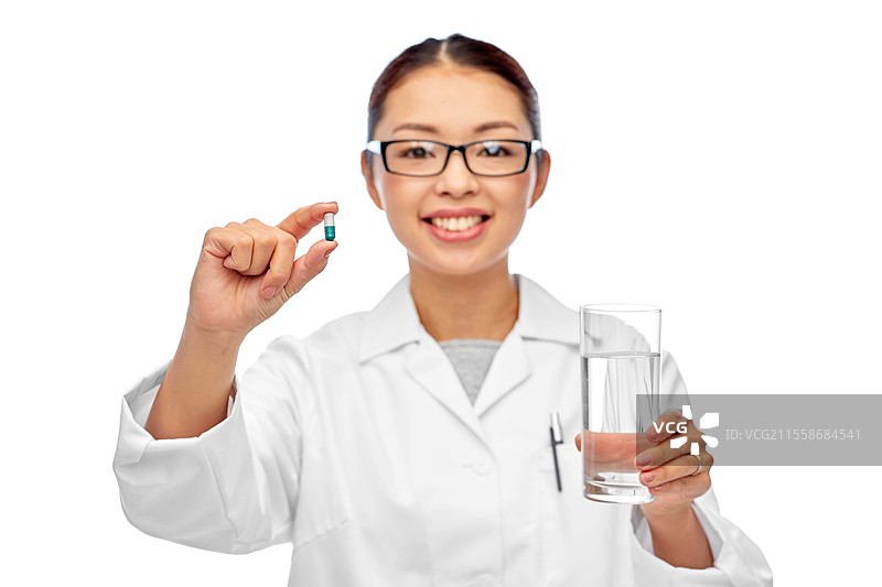 医学、职业和医疗保健概念 - 开心微笑的亚洲女性医生或护士手持药丸和一杯水，背景为白色。亚洲医生与药物和水杯。图片素材
