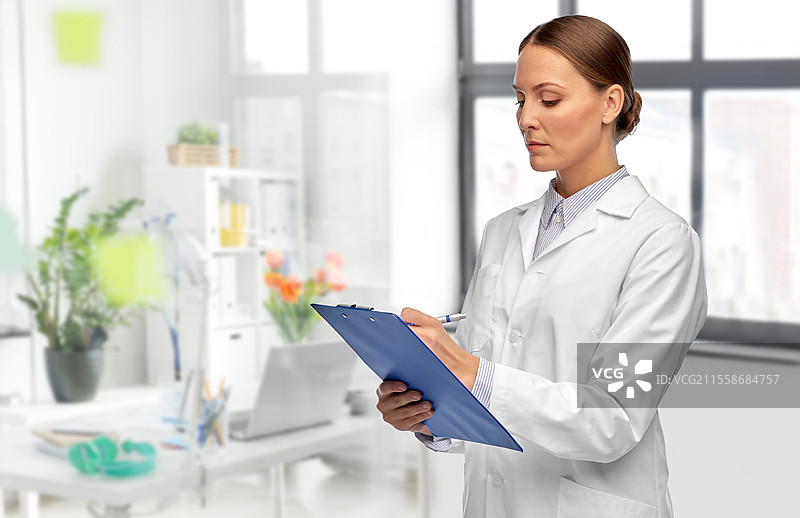 医学、职业和医疗保健概念 - 穿着白大褂的女医生在医院的医疗办公室背景下，手持夹板和笔撰写医疗报告。医院里的女医生与夹板。图片素材