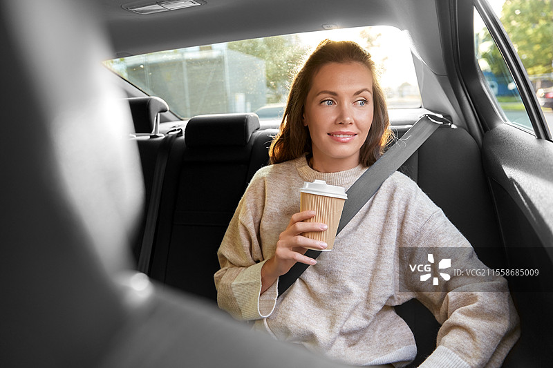 交通、车辆和人们的概念 - 开心微笑的女性乘客在出租车里喝外卖咖啡。微笑的女性乘客在车里喝咖啡。图片素材