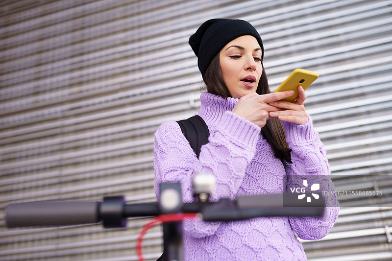 二十多岁的女性在户外骑电动滑板车，用智能手机录制语音备忘。生活方式概念。图片素材