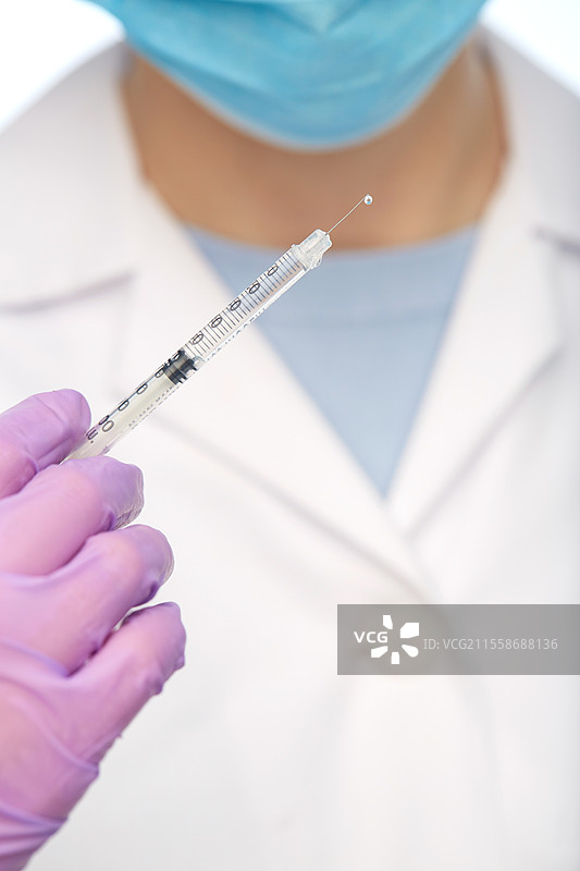 医学、疫苗接种和医疗保健概念 - 女性医生或护士手持注射器的特写，背景为白色。医生手持注射器的特写。图片素材
