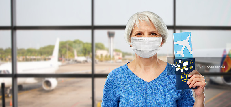 旅游、安全旅行和度假概念 - 戴着口罩的老年女性手持免疫护照和机票，背景为机场。戴着口罩的老年女性手持免疫护照和机票。图片素材