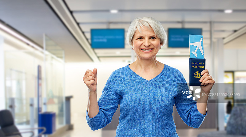 旅游、安全旅行和度假概念 - 开心的老年女性手持免疫护照和机票，背景为机场。老年女性手持免疫护照和机票。图片素材