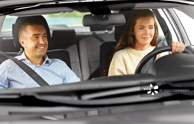 驾驶课程与人们的概念 - 汽车驾驶学校的教练正在教年轻女性驾驶。汽车驾驶学校的教练正在教女性。图片素材