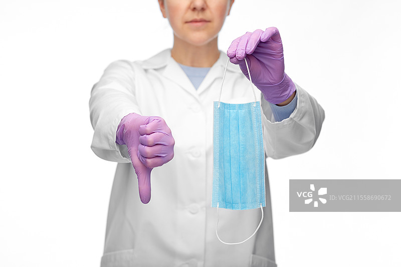 医学、健康保护和医疗保健概念 - 穿着白大褂和防护手套的女性医生在白色背景下竖起大拇指向下，戴着口罩的女性医生。图片素材