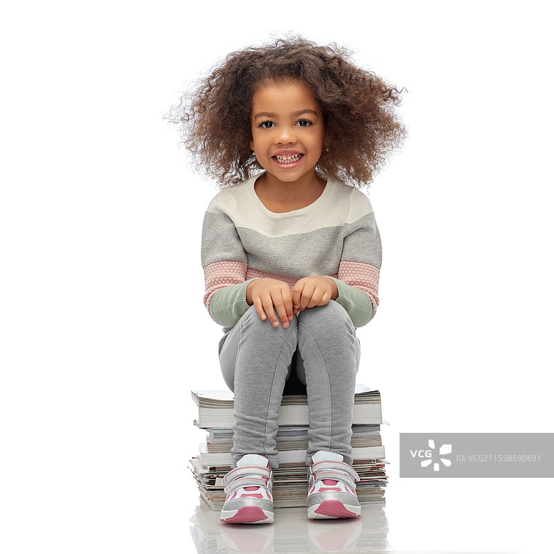 回收、垃圾分类和可持续发展概念 - 微笑的非裔美国女孩坐在一堆纸质杂志上，背景为白色。微笑的女孩正在分类纸张垃圾。图片素材