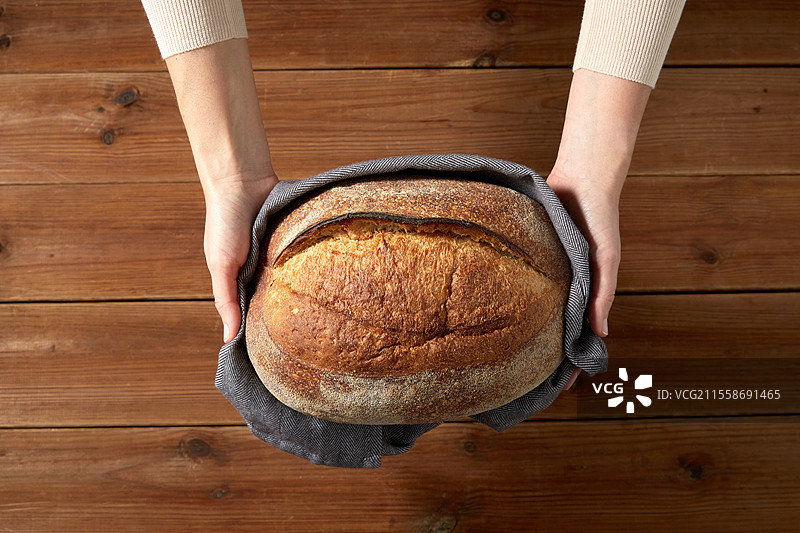 食品烹饪、烘焙和人们的概念 - 女性面包师在面包店或厨房中手持一条面包。女性面包师在面包店展示自制面包。图片素材