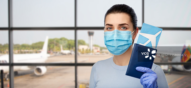 旅游、旅行和医疗保健概念 - 年轻女性佩戴口罩以防病毒疾病，手持机票和护照，背景为机场。戴着口罩的女性在机场手持护照和机票。图片素材