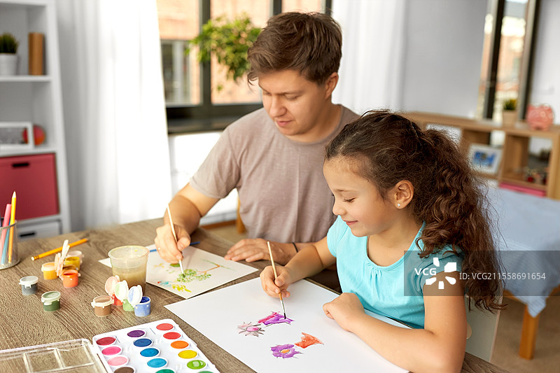 家庭、母亲和休闲的概念 - 快乐微笑的父亲在家中与他的小女儿共度时光，和她一起用彩色画画。快乐的父亲与小女儿在家中画画。图片素材