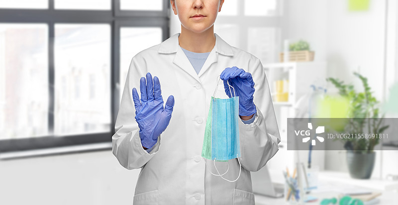 医疗、医学和疫情概念 - 女性医生或科学家戴着手套，手持两只口罩，在医院的医疗办公室背景下做出停止手势。女性医生用两只口罩做出停止手势。图片素材