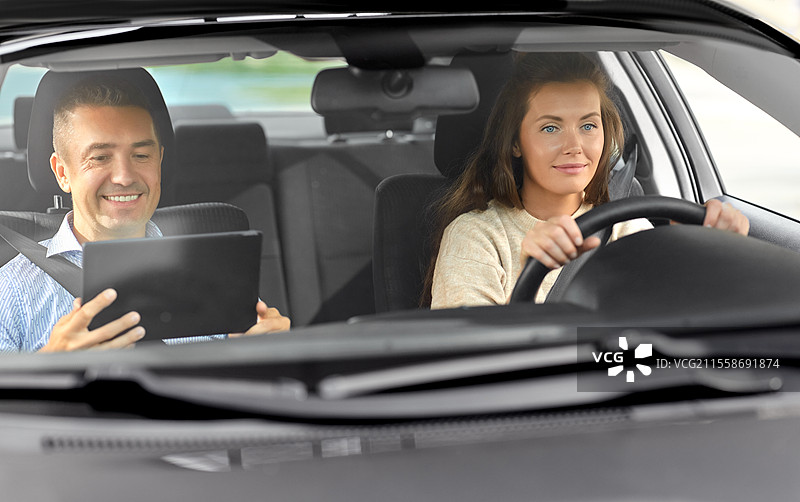 驾驶课程与人群概念 - 女士与驾驶学校教练在车内使用平板电脑交谈。女士与驾驶学校教练在车内交谈。图片素材