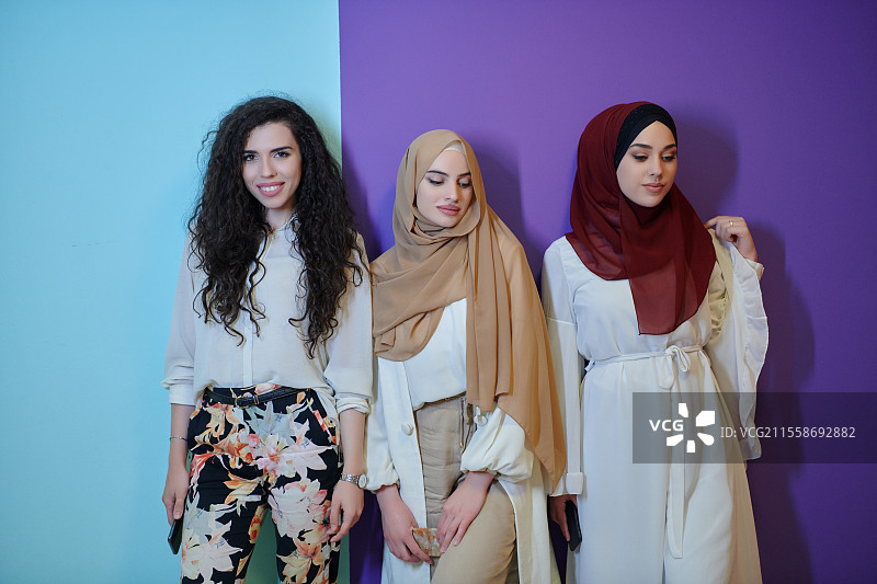 年轻的穆斯林女性在紫色和蓝色背景前摆姿势。快乐而美丽的女孩，两人戴着头巾，代表着斋月的概念。图片素材