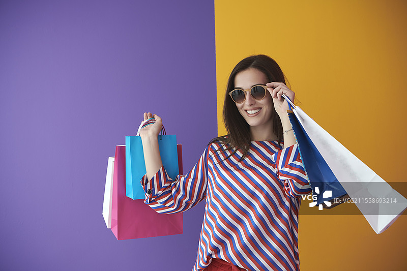 年轻女性手提购物袋，背景色彩斑斓。快乐的女孩在大促销后摆姿势展示新购买的商品。黑色星期五概念图片素材