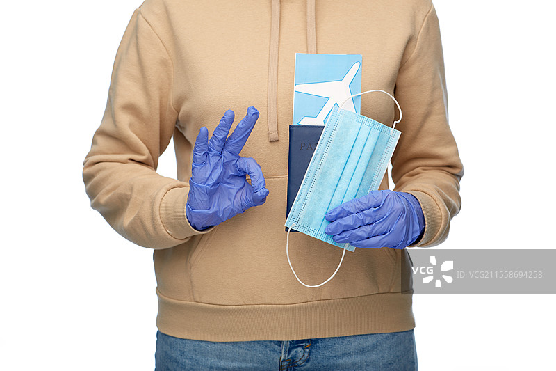 安全旅行、旅游和医疗保健概念 - 一位戴着口罩的女性手持护照和机票，背景为白色，做出“好”的手势。图片素材