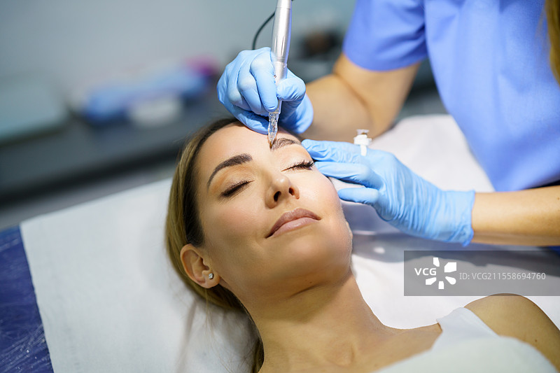 美容院中美丽女性的眉毛半永久化妆。美容师正在进行眉毛纹身的特写。微色素沉着治疗。图片素材