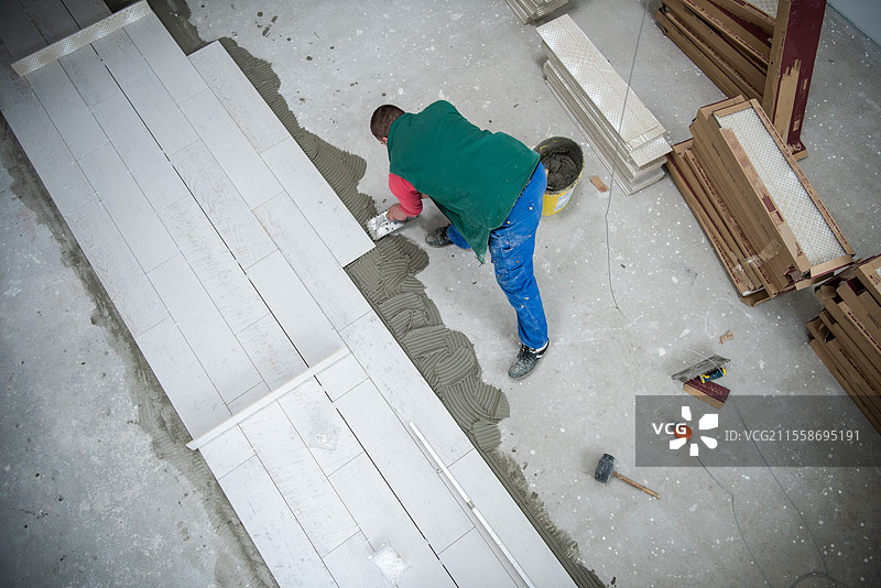 熟练工人在地板上安装陶瓷木纹效果瓷砖\n工人在新公寓的施工现场铺设复合地板图片素材
