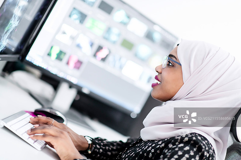 年轻的非裔美国现代穆斯林女商人，头戴围巾，在明亮的创意办公室中，面前有大屏幕。图片素材