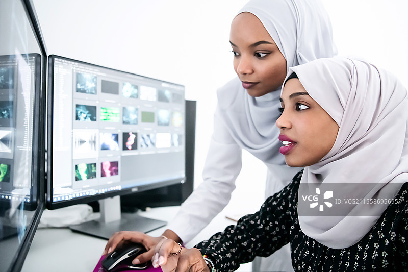 办公室里的朋友，两位年轻的非裔美国现代穆斯林女商人，佩戴着头巾，在明亮的创意办公环境中，背景有大屏幕。图片素材