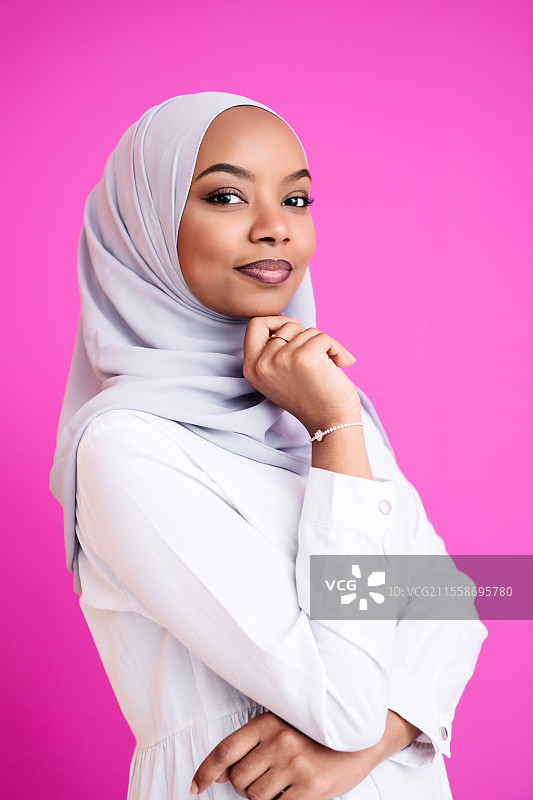 年轻现代穆斯林非洲美女穿着传统伊斯兰服装，背景为塑料粉色。图片素材