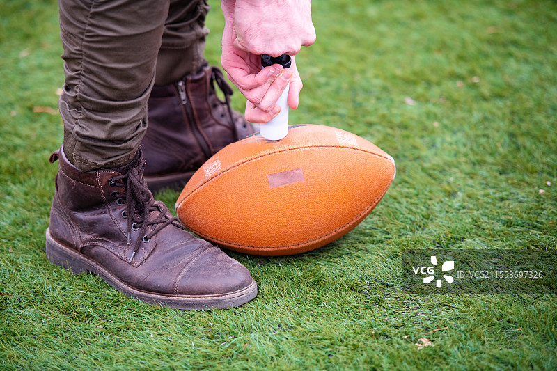 特写镜头：一名男子在球场上为美式足球充气图片素材