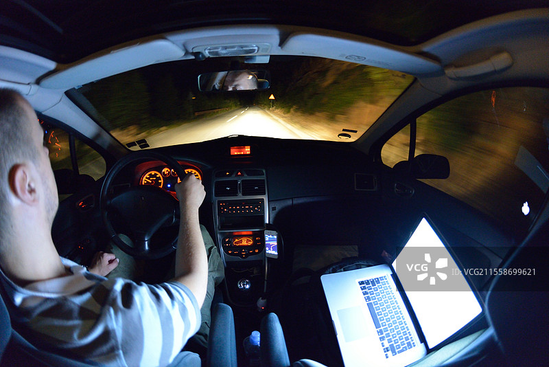 夜间驾驶时，一名男子一边开车一边使用笔记本电脑，并用智能手机进行导航。图片素材