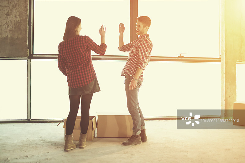 快乐的年轻休闲商务团队在新未完成的初创办公室大楼搬入时，阳光透过窗户照射，正搬运纸箱。图片素材