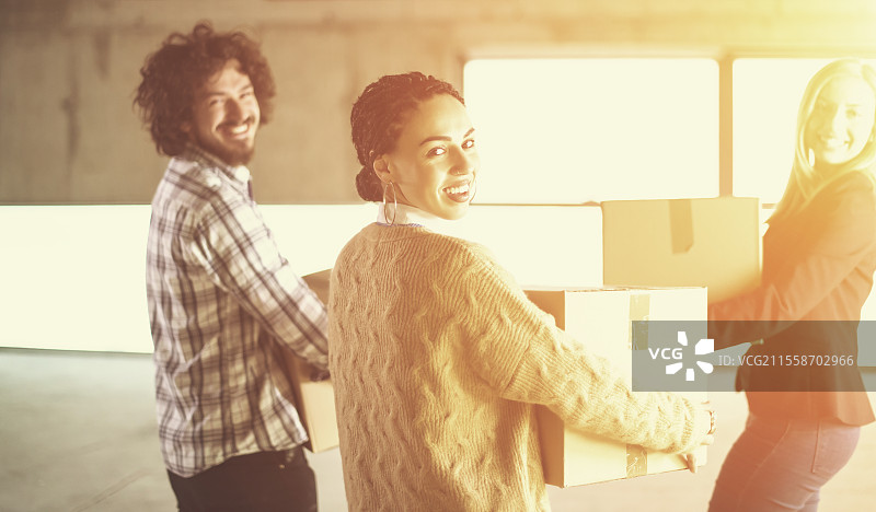 快乐的年轻休闲商务团队在新未完成的创业办公大楼搬入时，阳光透过窗户照射，搬运纸箱。图片素材