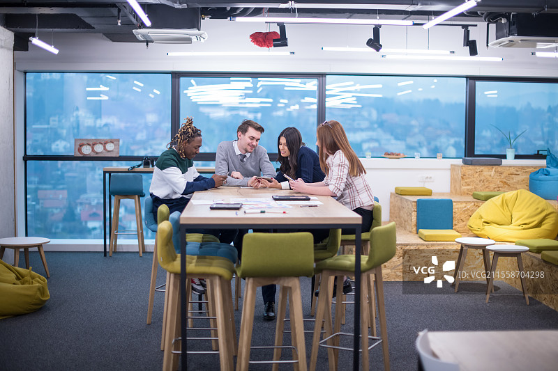 多元文化的初创企业团队在现代明亮的办公室内开会，进行头脑风暴，使用笔记本电脑和平板电脑工作。图片素材