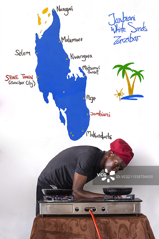 厨师在坦桑尼亚桑给巴尔东海岸的海滩上，墙上画着岛屿旅游地图，准备餐点。图片素材