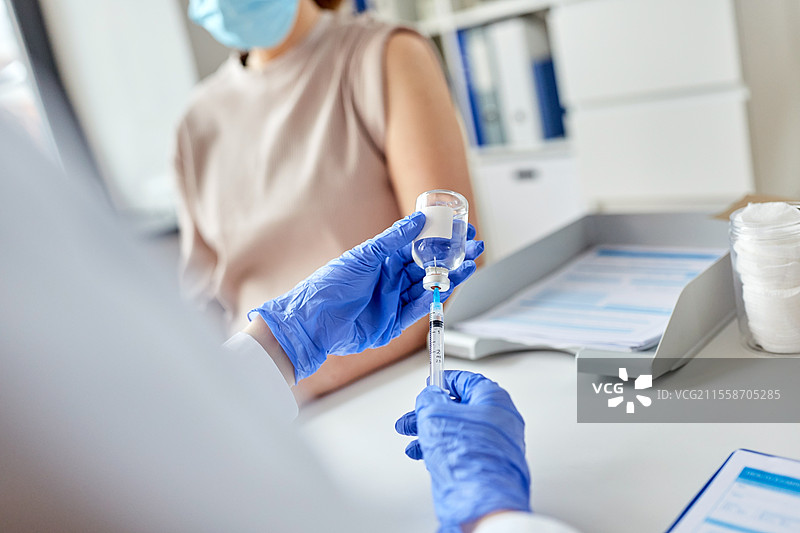 健康、医学和疫情概念 - 女性医生或护士佩戴防护口罩，使用注射器为患者接种疫苗。女性医生用注射器为患者接种疫苗。图片素材