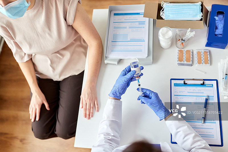 健康、医学和疫情概念 - 女性医生或护士佩戴防护口罩，使用注射器为患者接种疫苗。女性医生用注射器为患者接种疫苗。图片素材