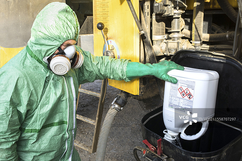 农民穿着化学防护服、手套和过滤口罩，在旋转洗涤头上冲洗罐子，以便将植物保护产品倒入喷雾器中。防护选择取决于风险、毒性程度和化学品的污染途径。图片素材