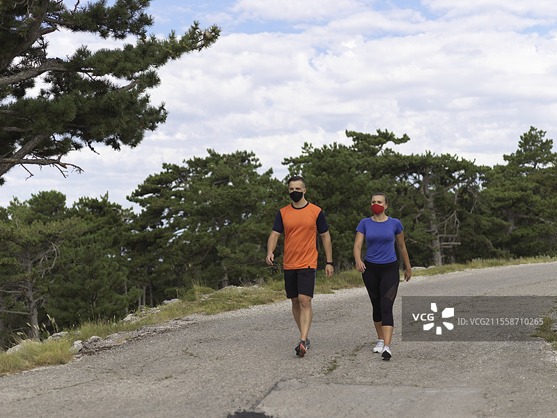 一对跑步者在早晨的自然环境中休息放松，准备装备和设置时间，佩戴着防护口罩。图片素材