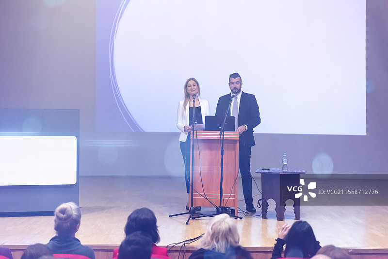 两位年轻的商务人士在会议室向坐在椅子上的同事们进行演讲图片素材