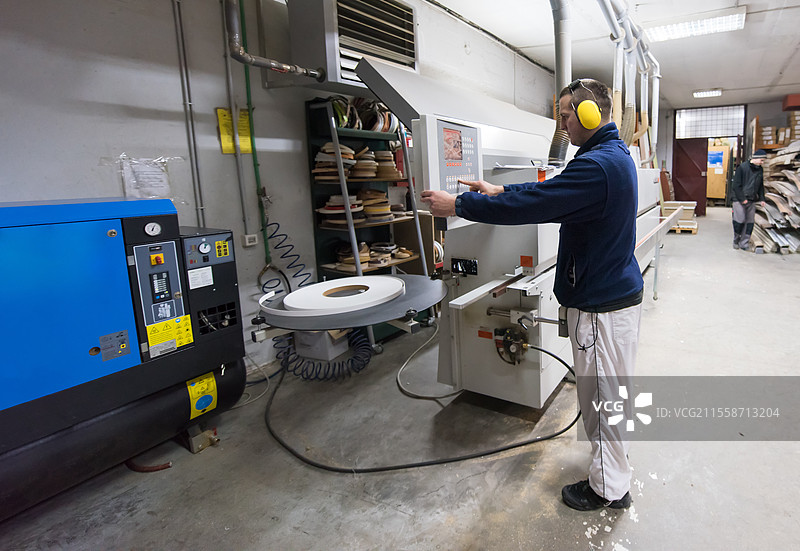 年轻的木匠在工作坊中计算和编程CNC木工机器。木工师傅正在为大型现代木工厂的CNC机器准备计算机程序。图片素材