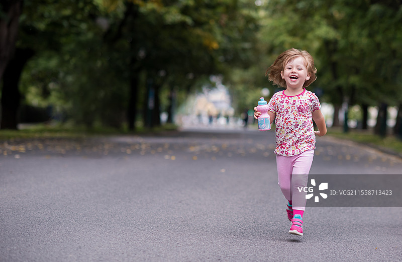 快乐的小女孩在城市公园跑步时喝着瓶装新鲜水。图片素材