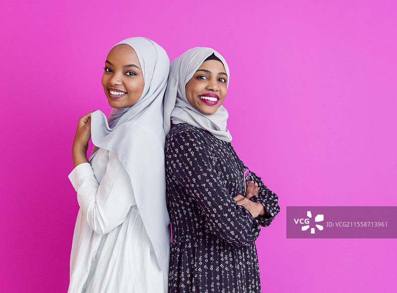 两位年轻现代穆斯林非洲美女穿着传统伊斯兰服装，背景为塑料粉色。图片素材
