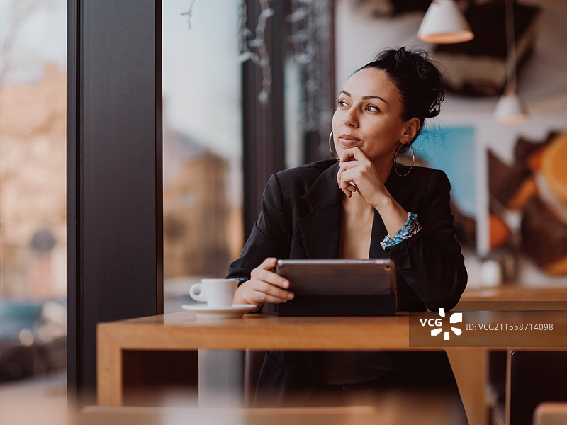 拉丁裔女性在咖啡馆里坐着，使用平板电脑，喝着咖啡，享受工作间隙。图片素材