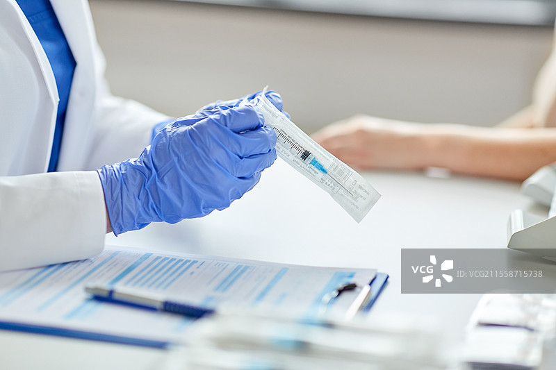 健康、医学和疫情概念 - 女医生或护士特写，戴着防护手套，打开疫苗注射器的包装，准备为医院里的病人接种。女医生手持注射器与病人在医院。图片素材